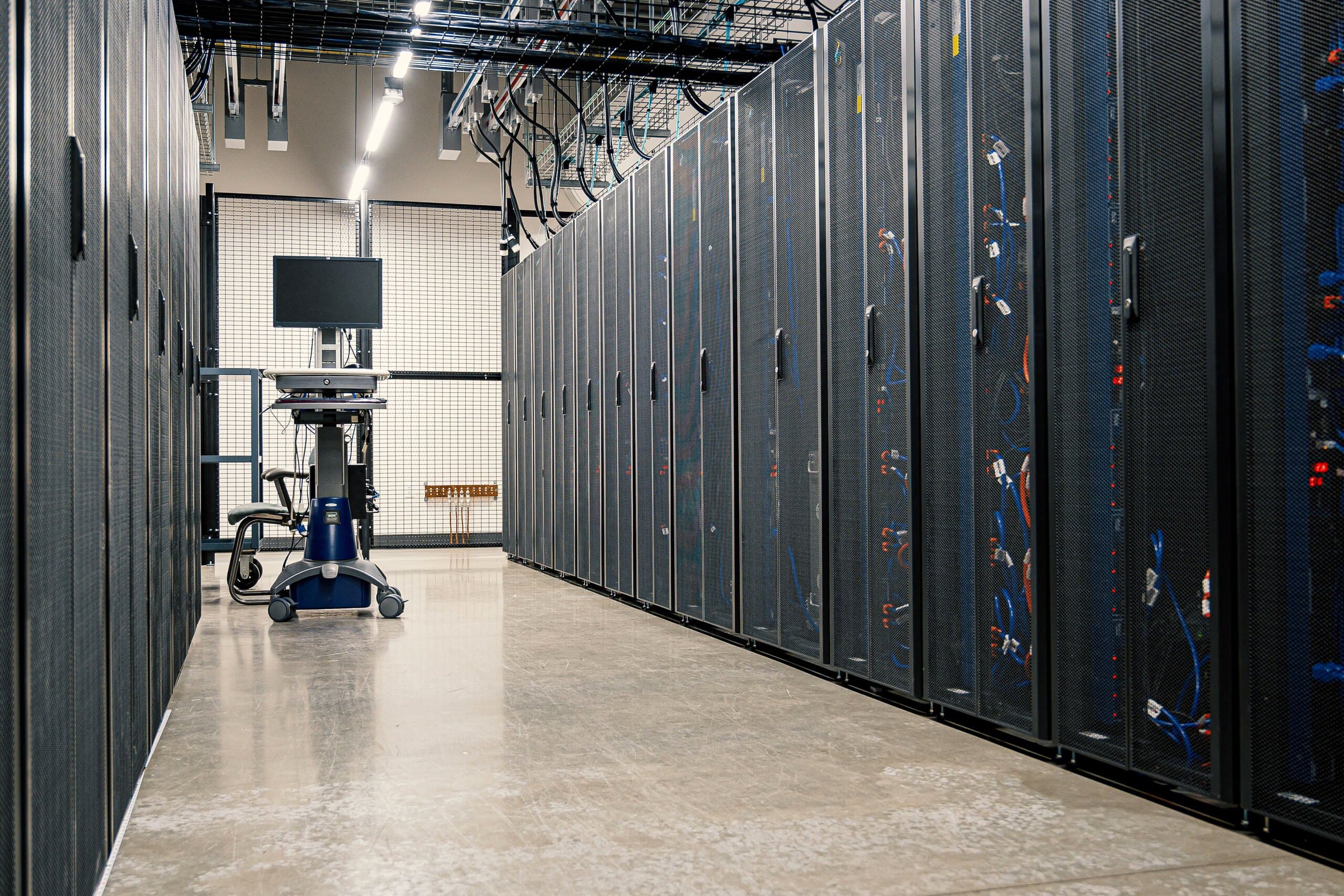 An aisle of server cabinets in a data hall, with cable trays overhead